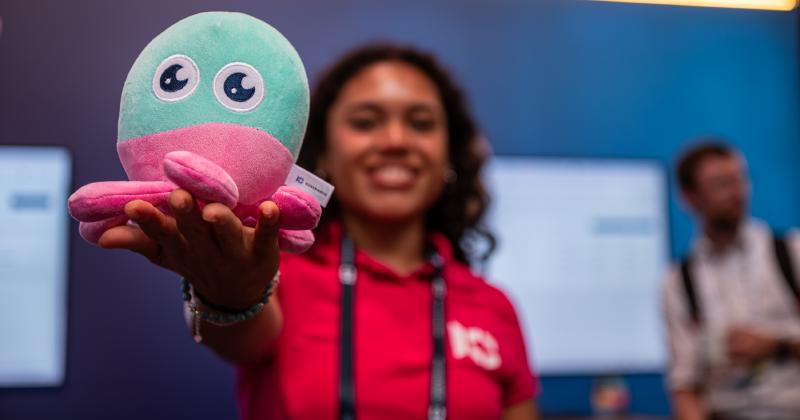 Kubermatic team member holding the company's pink and teal octopus mascot plush toy at the ContainerDays Hamburg 2026 booth